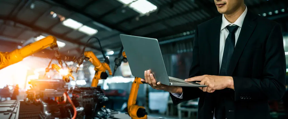 man holding laptop with background manufacturing machines